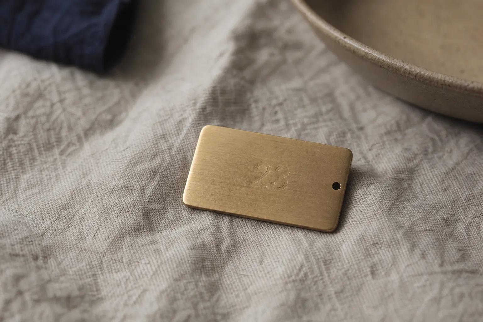A small brass card engraved with a two-digit number resting on oatmeal linen.