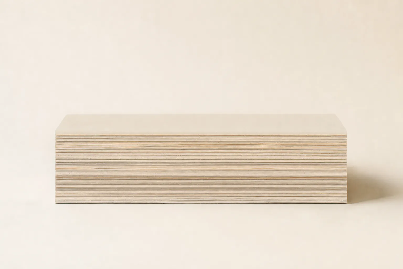 The STRATA pillow seen side-on as a low, wide block, its fine layer edges running along the side and its top plain, on a warm off-white ground.